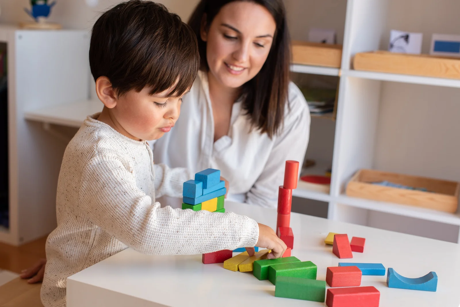 kid-playing-with-wood-blocks-and-teacher-educador-help-